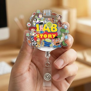 May include: A colorful badge reel featuring characters from the animated film "Toy Story." The design includes Buzz Lightyear, Woody, and other characters, with the words "Lab Story" in yellow and blue. The reel has a clear plastic strap and a retractable cord.