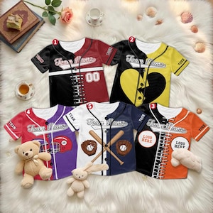 May include: Five baseball jerseys in various colors, including black, red, orange, yellow, white, and purple. Each jersey features the text "Team Name" and other baseball-themed graphics. Some jerseys have the text "YOUR" and "LOGO HERE".