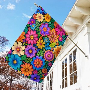 May include: A rectangular outdoor flag featuring a vibrant, dense pattern of multi-colored flowers in shades of pink, orange, yellow, blue, and purple, interspersed with green leaves against a dark background, mounted on a metal pole.