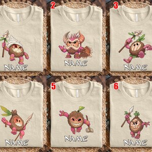 Puede incluir: Camisetas beige con dise&ntilde;os de personajes de dibujos animados. Cada camiseta presenta un personaje diferente con una expresi&oacute;n &uacute;nica y sosteniendo varios objetos. La palabra "NAME" est&aacute; impresa debajo de cada personaje. Las camisetas se muestran sobre una superficie tejida.