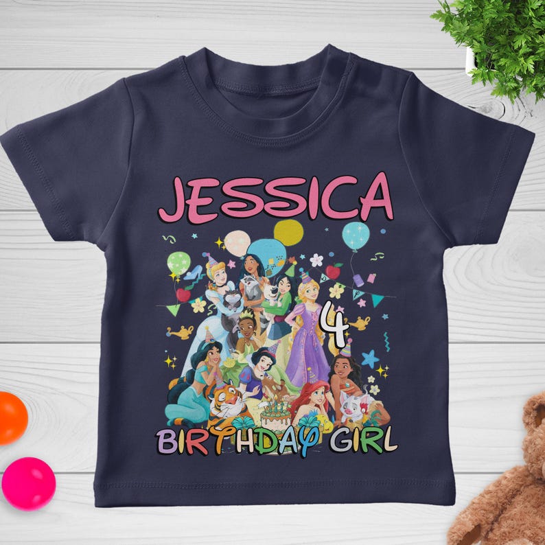 May include: Navy blue t-shirt featuring a colorful graphic of Disney princesses, the name "JESSICA", the number "4", and the text "BIRTHDAY GIRL". The design includes balloons and confetti. A fun, festive shirt for a birthday celebration.
