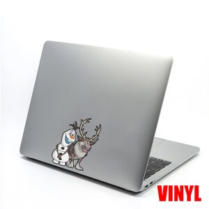 Puede incluir: Un port&aacute;til plateado con una pegatina de vinilo con Olaf el mu&ntilde;eco de nieve y Sven el reno de la pel&iacute;cula Frozen. La pegatina est&aacute; en la esquina superior izquierda del port&aacute;til. La palabra "VINYL" est&aacute; impresa en rojo en la esquina inferior derecha.