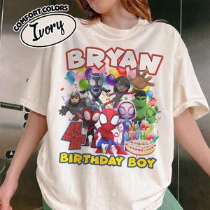 May include: An ivory t-shirt featuring a graphic print with the text "BRYAN" at the top and "4 BIRTHDAY BOY" at the bottom. The design includes various superhero characters, colorful balloons, and a birthday cake with "HAPPY BIRTHDAY" text.