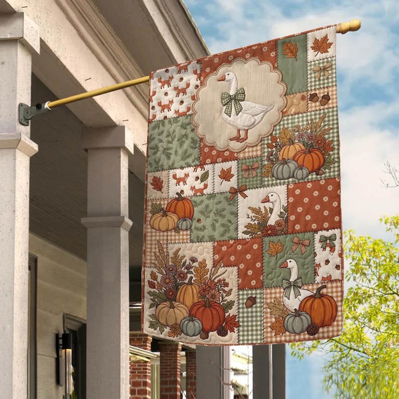 Pu&ograve; includere: Una bandiera da giardino rettangolare con un design patchwork a tema autunnale. La bandiera mostra illustrazioni di oche bianche con fiocchi verdi, zucche arancioni, ghiande e foglie autunnali nei toni del verde, dell'arancione e del marrone.