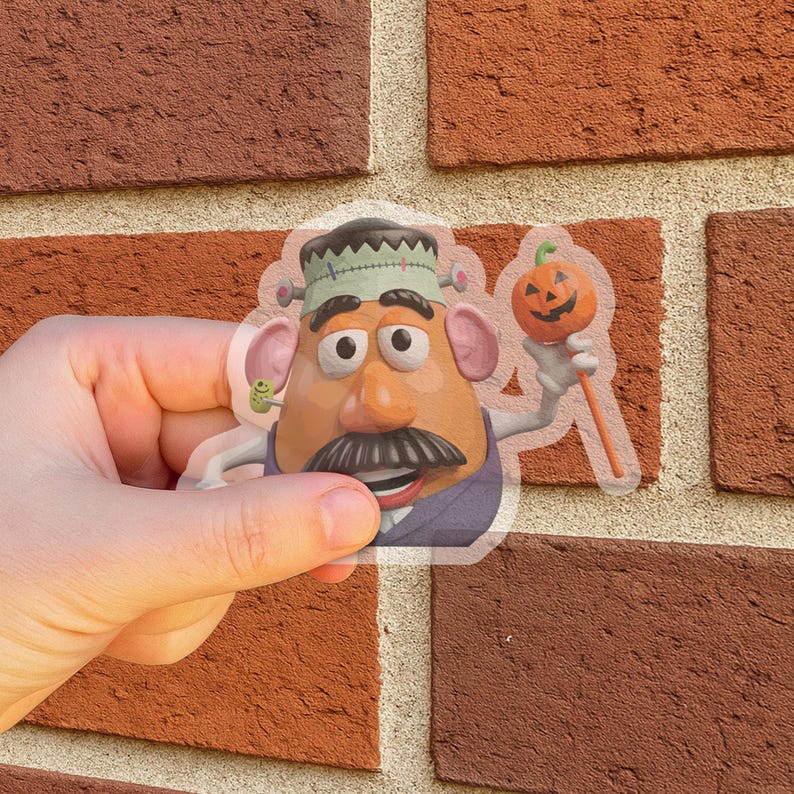 May include: A clear sticker of a cartoon character in a Frankenstein costume, holding a jack-o'-lantern. The character has a large moustache, a green bolt in its ear, and a stitched-up head. The sticker is held against a brick wall.