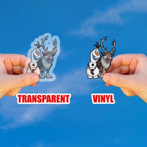 Puede incluir: Dos pegatinas con personajes de la pel&iacute;cula animada "Frozen" se sostienen contra un cielo azul. Una es transparente, la otra de vinilo. El texto de la imagen dice "TRANSPARENT" y "VINYL".