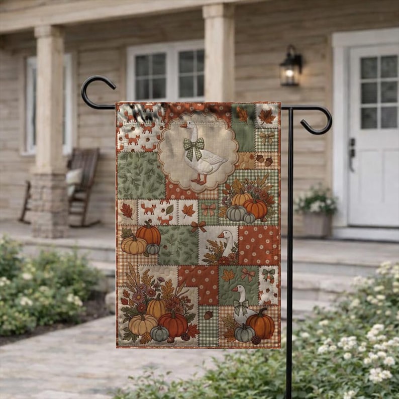 Pu&ograve; includere: Una bandiera da giardino rettangolare con un design patchwork a tema autunnale. Il motivo presenta illustrazioni di oche bianche con fiocchi verdi, zucche arancioni, ghiande marroni e foglie autunnali nei toni del verde, dell'arancione e del marrone.