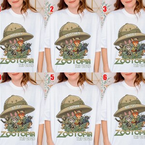 May include: White t-shirts with a Zootopia graphic. Each shirt has a different word on the safari hat: "Mommy", "Brother", "Daddy", "Lil Sis", "Sophie", and "Big Sis". The text "Zootopia Trip 2026" is below the graphic. The shirts are for a family trip.