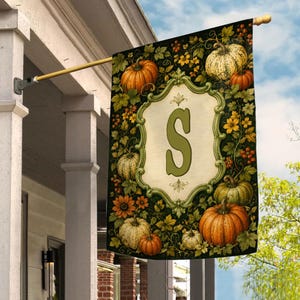 May include: A rectangular garden flag featuring a central cream-colored ornate frame with a large green letter S. The background is decorated with various pumpkins, orange sunflowers, green leaves, and small red berries on a dark green backdrop.