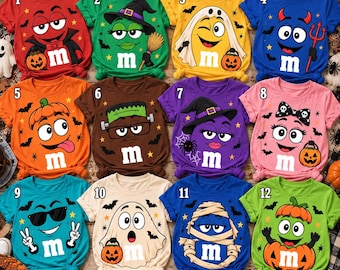 May include: A collection of twelve colorful t-shirts featuring M&M characters dressed in various Halloween costumes including a vampire, witch, ghost, devil, pumpkin, Frankenstein, mummy, and a character with sunglasses, all decorated with bats and stars.