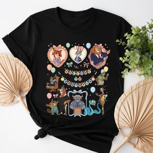 K&ouml;nnte beinhalten: Schwarzes T-Shirt mit Cartoon-Charakteren aus Zootopia, darunter Nick Wilde, Judy Hopps und B&uuml;rgermeister Lionheart, umgeben von Luftballons und dem Text "Welcome to Zootopia". Das Design ist farbenfroh und skurril, perfekt f&uuml;r Fans des Animationsfilms.
