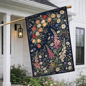May include: A decorative garden flag featuring a floral design with tulips, foxgloves, daisies, and hummingbirds on a navy blue background. The flag is rectangular and hangs from a wooden pole, adding a touch of nature-inspired decor to any outdoor space.