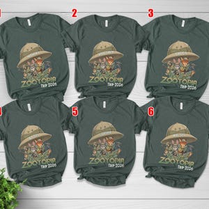 May include: Dark green t-shirts featuring a safari hat graphic and the text "ZOOTOPIA TRIP 2026". The shirts are labelled "Mommy", "Brother", "Daddy", "By Sis", "Sophie", and "Big Sis".