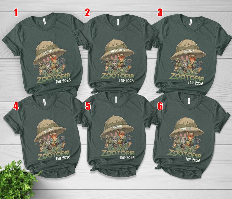 May include: Dark green t-shirts featuring a safari hat graphic and the text "ZOOTOPIA TRIP 2026". The shirts are labelled "Mommy", "Brother", "Daddy", "By Sis", "Sophie", and "Big Sis".