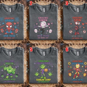 May include: Six dark grey t-shirts with superhero designs. Each shirt features a different character: Spider-Man, Spider-Gwen, Spider-Spin, Hulk, Green Goblin, and Iron Man. Text includes character names and phrases like "Web-Head" and "Smash-Head."