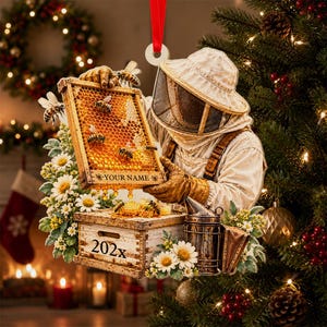 May include: A hanging Christmas ornament featuring a beekeeper in protective gear holding a honeycomb frame with bees. The frame includes the text YOUR NAME and a wooden box base labeled 202x, decorated with white daisies and a metal smoker.