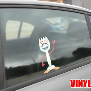 May include: A white vinyl decal of the character Forky from the animated film Toy Story. Forky is waving with a smiling expression. The decal is affixed to a car window. The word "VINYL" is printed in red.