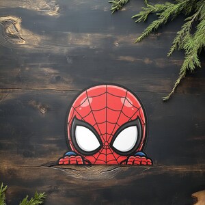 May include: A red and black Spider-Man mask graphic with white eye lenses. The graphic is peeking over a dark wooden surface, with green sprigs in the background. The mask features a web design.