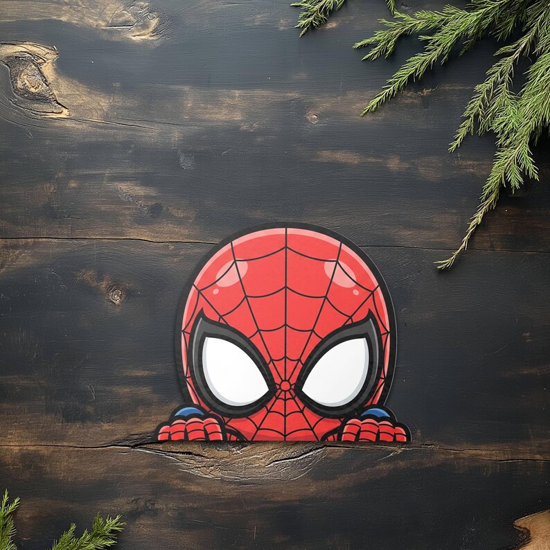 May include: A red and black Spider-Man mask graphic with white eye lenses. The graphic is peeking over a dark wooden surface, with green sprigs in the background. The mask features a web design.