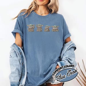 Puede incluir: Una camiseta de color azul vaquero con un estampado gr&aacute;fico de cuatro peque&ntilde;as criaturas verdes con orejas grandes y t&uacute;nicas color canela en varias poses. La camiseta tiene mangas cortas y cuello redondo. Una etiqueta dice COMFORT COLORS Blue Jean.