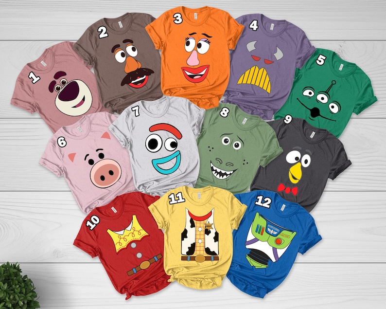 May include: A collection of twelve short-sleeved t-shirts in various colors, each featuring a graphic print of a character face or costume design from the Toy Story franchise, numbered one through twelve and arranged in a heart-shaped layout.