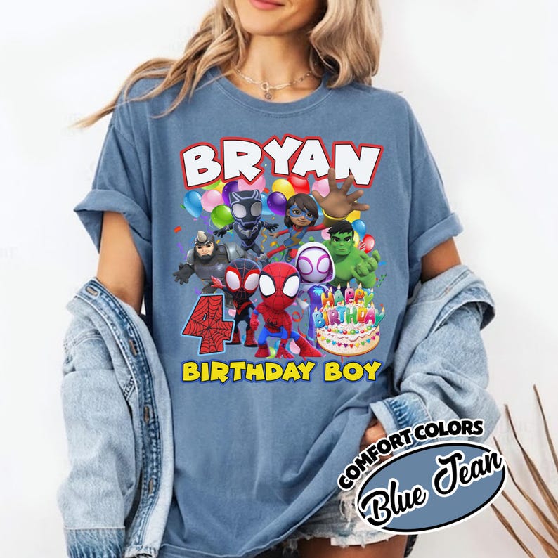 May include: A blue jean colored t-shirt featuring a graphic print of various superhero characters, colorful balloons, a birthday cake, and the text "BRYAN" at the top and "4 BIRTHDAY BOY" at the bottom. The shirt has short sleeves and a crew neckline.