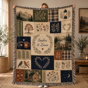 May include: A woven throw blanket featuring a patchwork design with nature-themed illustrations including mountains, trees, a cabin, birds, mugs, and a lantern. The center panel displays the text Sophia & Lucas surrounded by a leafy wreath.