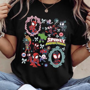May include: Black t-shirt featuring a colorful graphic of Spider-Man and other characters from the Spidey and His Amazing Friends series. The design includes the text "Spidey Amazing Friends" and various web and spider motifs.