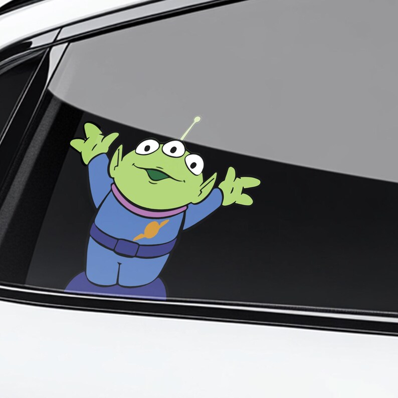 May include: A green alien character sticker with three eyes, wearing a blue uniform with a yellow emblem. The sticker is applied to a car window, with the alien's arms raised in a welcoming gesture.