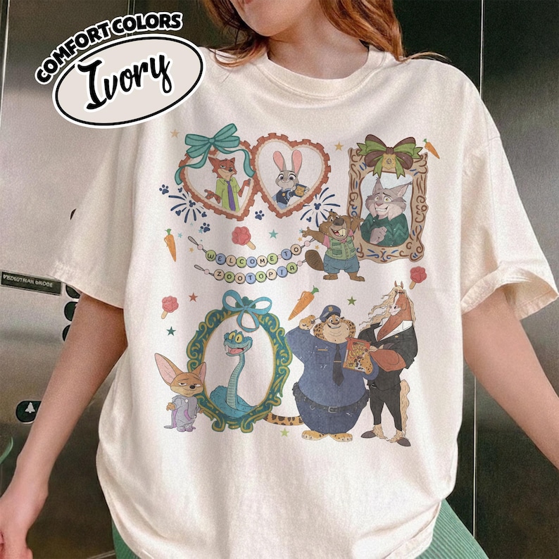 May include: An ivory short-sleeve t-shirt featuring a graphic print of Zootopia characters including Nick, Judy, and others framed in decorative hearts and ovals. The design includes the text Welcome to Zootopia, carrots, and small stars.