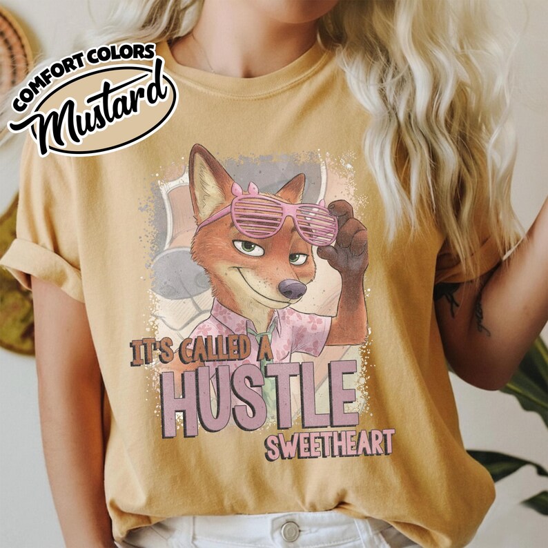 Puede incluir: Una camiseta color amarillo mostaza con un gr&aacute;fico de un zorro de dibujos animados con gafas de sol de persiana rosas y una camisa estampada. El texto dice IT'S CALLED A HUSTLE SWEETHEART. Un logo circular muestra COMFORT COLORS MUSTARD.