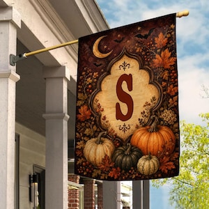May include: A rectangular garden flag featuring a central cream-colored ornate frame with a large dark red letter S. The design includes orange and green pumpkins, autumn leaves, berries, a crescent moon, and black bats on a dark background.