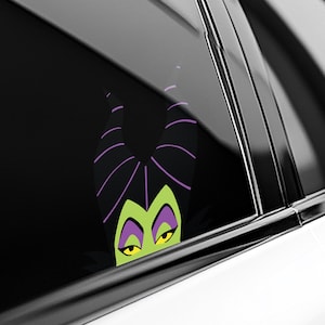 May include: A black and green vinyl car decal featuring the character Maleficent. The decal shows Maleficent's face with her signature horns, green skin, and yellow eyes. The horns are black with purple stripes.