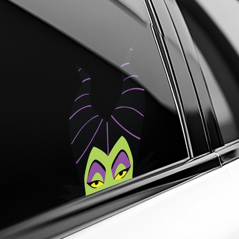 May include: A black and green vinyl car decal featuring the character Maleficent. The decal shows Maleficent's face with her signature horns, green skin, and yellow eyes. The horns are black with purple stripes.