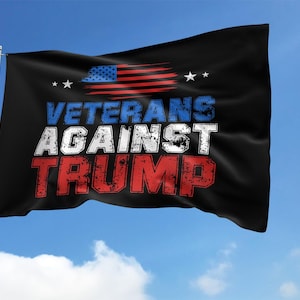 May include: Black flag with the text "VETERANS AGAINST TRUMP" in white, blue, and red. The flag also features a distressed American flag design and two white stars. The flag is waving in the wind against a blue sky.