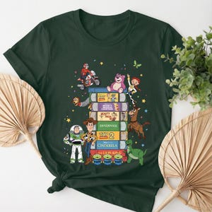 Może przedstawiać: Ciemnozielona koszulka z wieżą książek z filmami Disneya z postaciami z Toy Story. Projekt zawiera Buzza Astrala, Chudego i inne postacie z film&oacute;w. Koszulka jest wygodna i nadaje się do noszenia na co dzień.