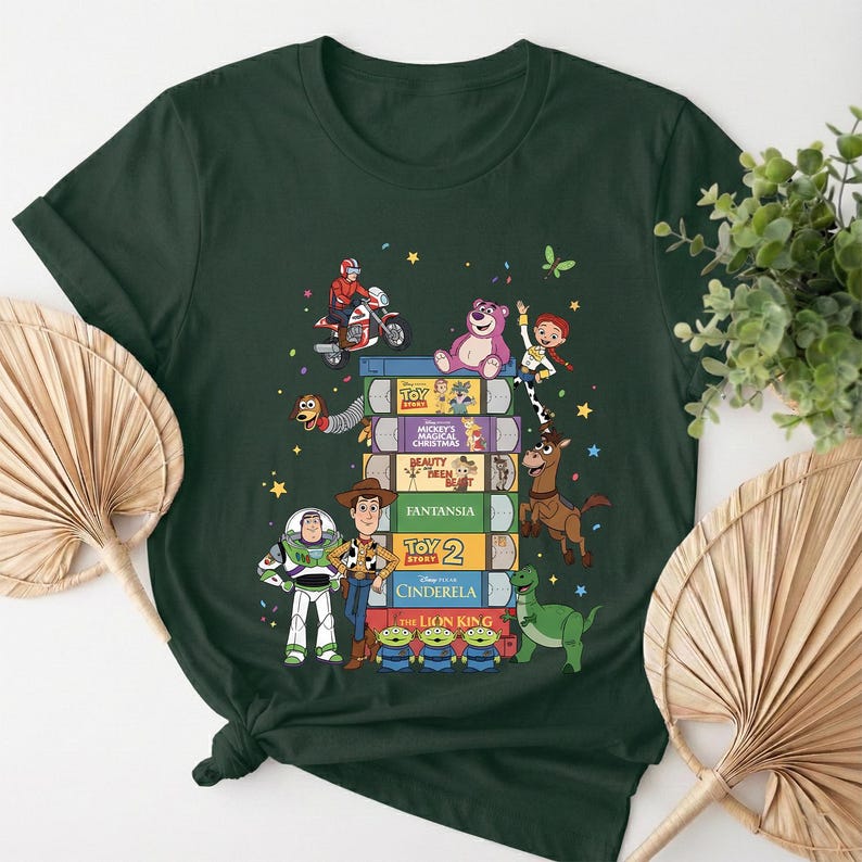 Może przedstawiać: Ciemnozielona koszulka z wieżą książek z filmami Disneya z postaciami z Toy Story. Projekt zawiera Buzza Astrala, Chudego i inne postacie z film&oacute;w. Koszulka jest wygodna i nadaje się do noszenia na co dzień.