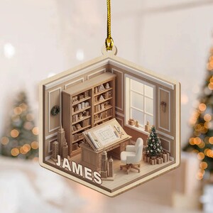 May include: A hexagonal wooden ornament featuring a 3D-style illustration of an office with bookshelves, a drafting desk, a white chair, a small Christmas tree, and miniature skyscrapers. The name JAMES is printed in white at the bottom.