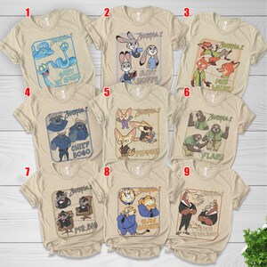 Pode incluir: Uma cole&ccedil;&atilde;o de nove camisetas bege com personagens do filme de anima&ccedil;&atilde;o "Zootopia 2". Cada camiseta apresenta um personagem ou grupo de personagens diferentes com seus nomes. As camisetas t&ecirc;m mangas curtas e gola redonda.