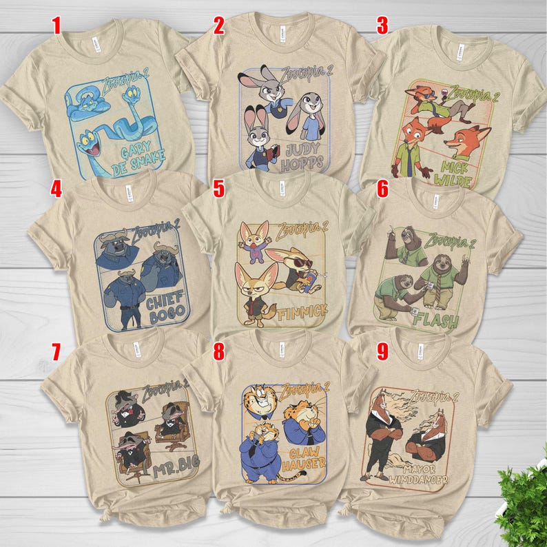 Pode incluir: Uma cole&ccedil;&atilde;o de nove camisetas bege com personagens do filme de anima&ccedil;&atilde;o "Zootopia 2". Cada camiseta apresenta um personagem ou grupo de personagens diferentes com seus nomes. As camisetas t&ecirc;m mangas curtas e gola redonda.