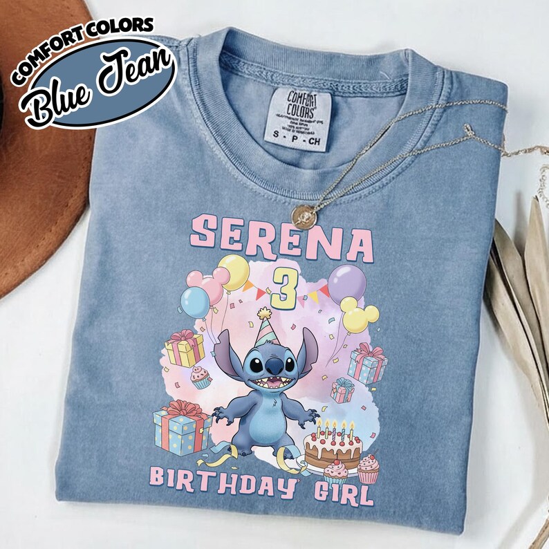 Peut inclure: Un t-shirt bleu jean avec une illustration du personnage Stitch portant un chapeau de f&ecirc;te, entour&eacute; de ballons, de cadeaux et d'un g&acirc;teau d'anniversaire. Le texte indique SERENA 3 BIRTHDAY GIRL. Le t-shirt porte une &eacute;tiquette Comfort Colors.