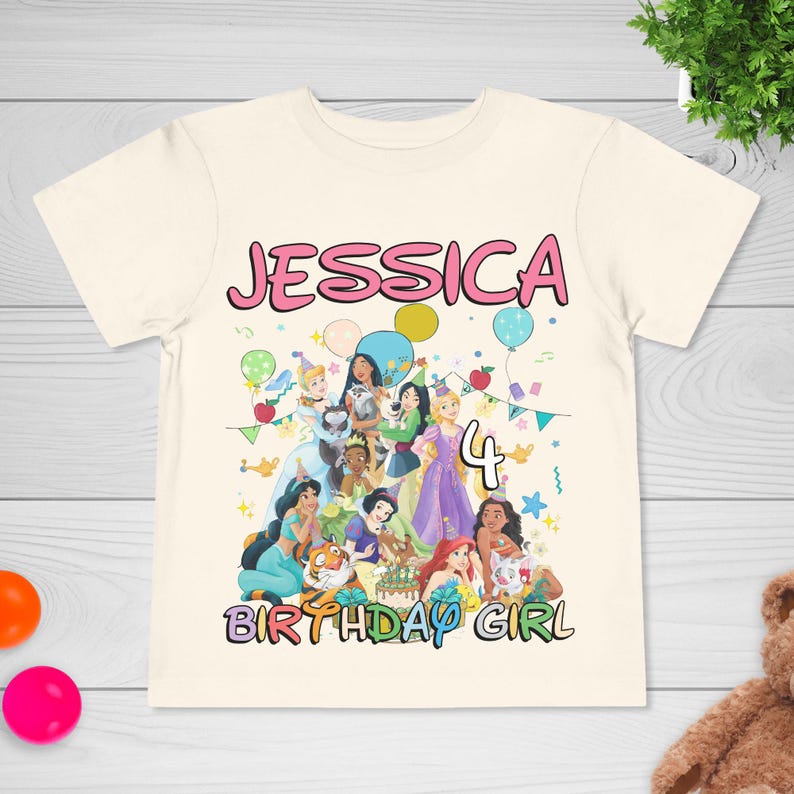 May include: Cream-colored t-shirt featuring a group of cartoon princesses. The name "JESSICA" is printed in pink above the princess graphic, with the number "4" and the words "BIRTHDAY GIRL" below. Balloons and confetti are also included in the design.