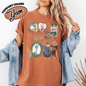 May include: A rust-colored t-shirt featuring a graphic print of various animated animal characters from Zootopia, including Nick Wilde, Judy Hopps, and others, with the text "WELCOME TO ZOOTOPIA" and a "COMFORT COLORS" logo in the corner.