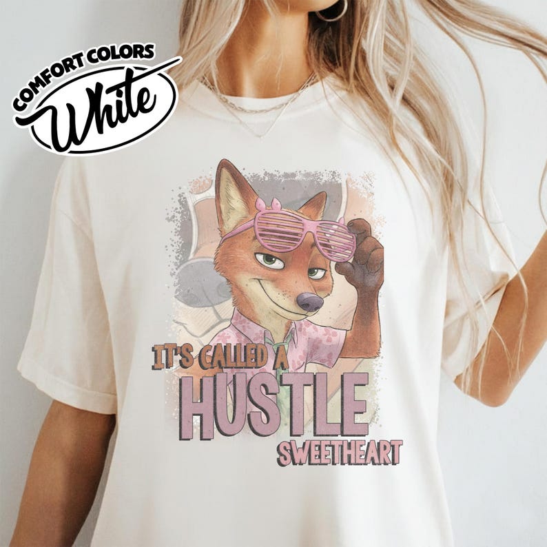 Puede incluir: Una camiseta blanca con el gr&aacute;fico de un zorro que lleva gafas de sol de persiana rosas y una camisa floral. El texto dice IT'S CALLED A HUSTLE SWEETHEART. Un logo en la esquina superior izquierda dice COMFORT COLORS White. Dise&ntilde;o desgastado.