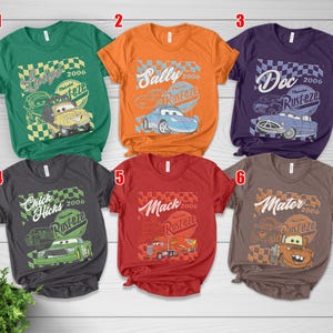 May include: Six short-sleeved t-shirts in various colors, each featuring a graphic from the animated film "Cars." Designs include characters like Lightning McQueen, Sally, Doc Hudson, Chick Hicks, Mack, and Mater, with the "Rust-eze" logo.