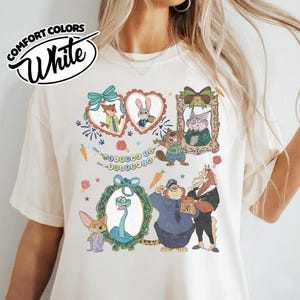 May include: A white t-shirt featuring a graphic print of Zootopia characters including Nick Wilde, Judy Hopps, and others framed in decorative hearts and ornate borders, with a banner reading Welcome to Zootopia and small carrot icons.
