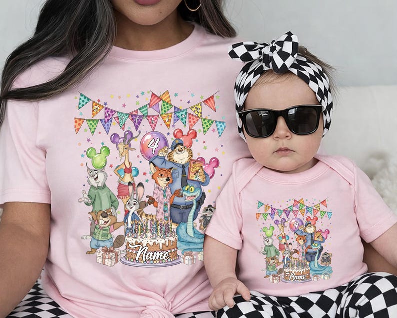 May include: Pink t-shirt and baby bodysuit set featuring a colorful cartoon illustration of animal characters, a birthday cake, and festive bunting. The t-shirt is worn by an adult, and the bodysuit is worn by a baby.