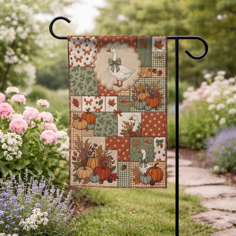 Pu&ograve; includere: Una bandiera da giardino rettangolare con un design patchwork a tema autunnale. Il motivo presenta illustrazioni di oche bianche con fiocchi verdi, zucche arancioni, ghiande marroni e foglie autunnali nei toni dell'arancione, verde e marrone.