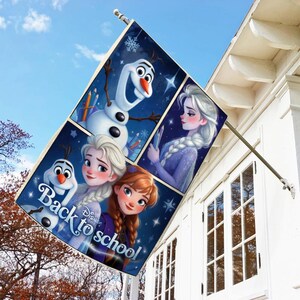 May include: A rectangular flag featuring characters from the Disney movie Frozen. The flag has a blue background with images of Olaf, Elsa, and Anna, with the text "Back to school". The flag is mounted on a white house.