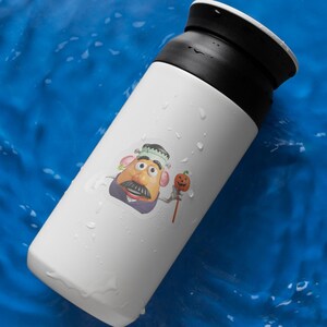 May include: White travel mug with a black lid. A sticker of a cartoon character with a moustache, wearing a Frankenstein-themed hat and holding a pumpkin on a stick is on the side. The mug is on a blue surface.